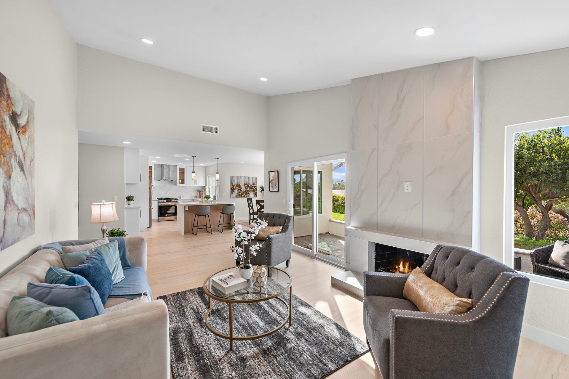 Vaulted living room with marble slab fireplace wall opening to a renovated kitchen