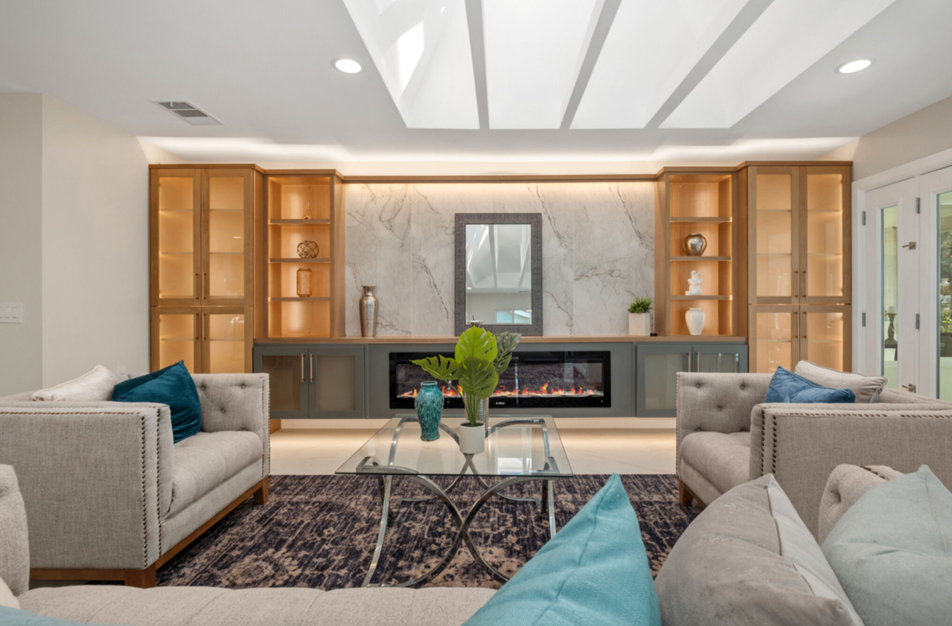 Entertainment wall with marble slab surround, linear fireplace, and lighted wood display cabinetry under skylights