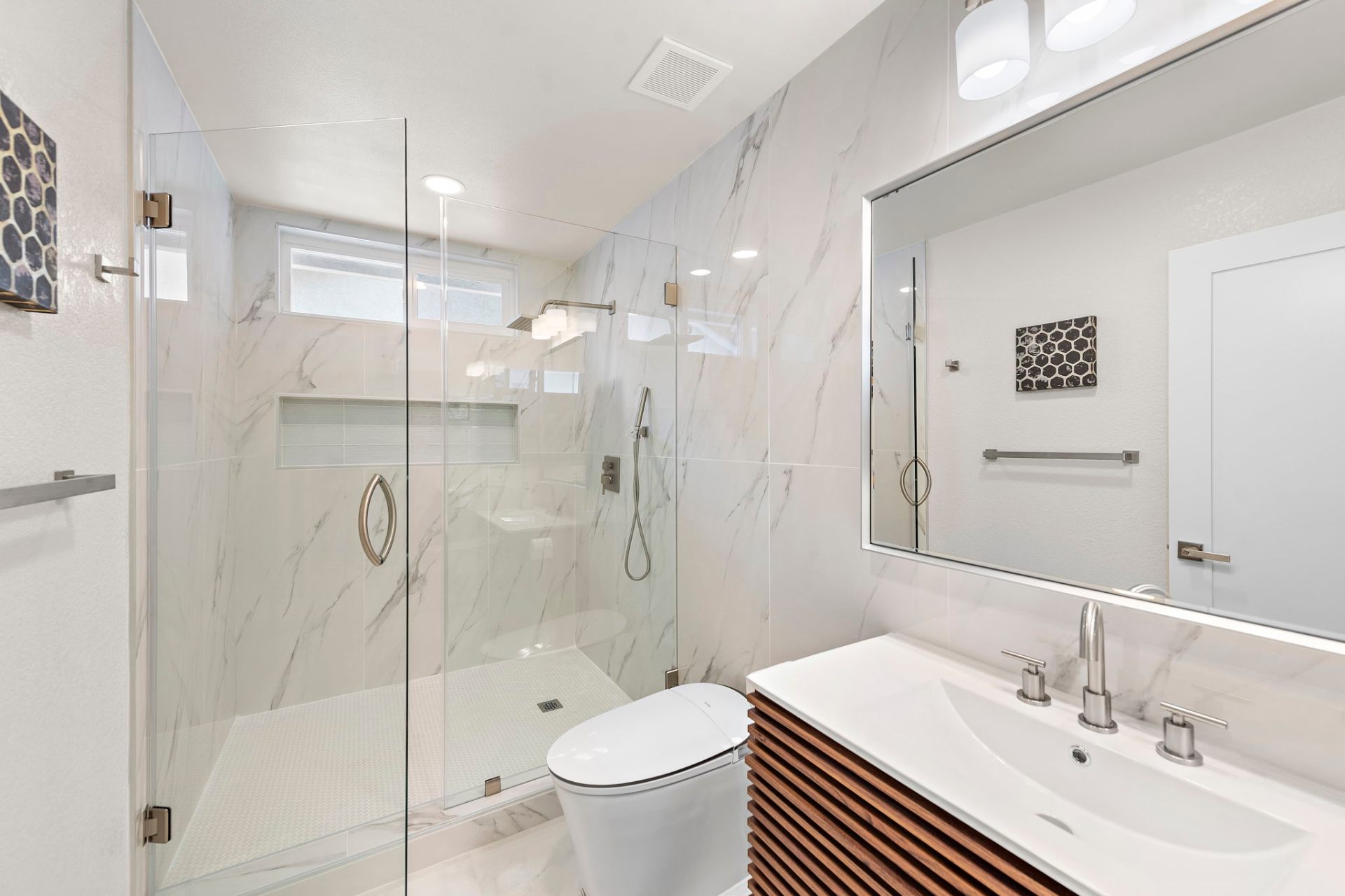 Bright marble bathroom with frameless glass shower, walnut vanity, and honeycomb tile accent
