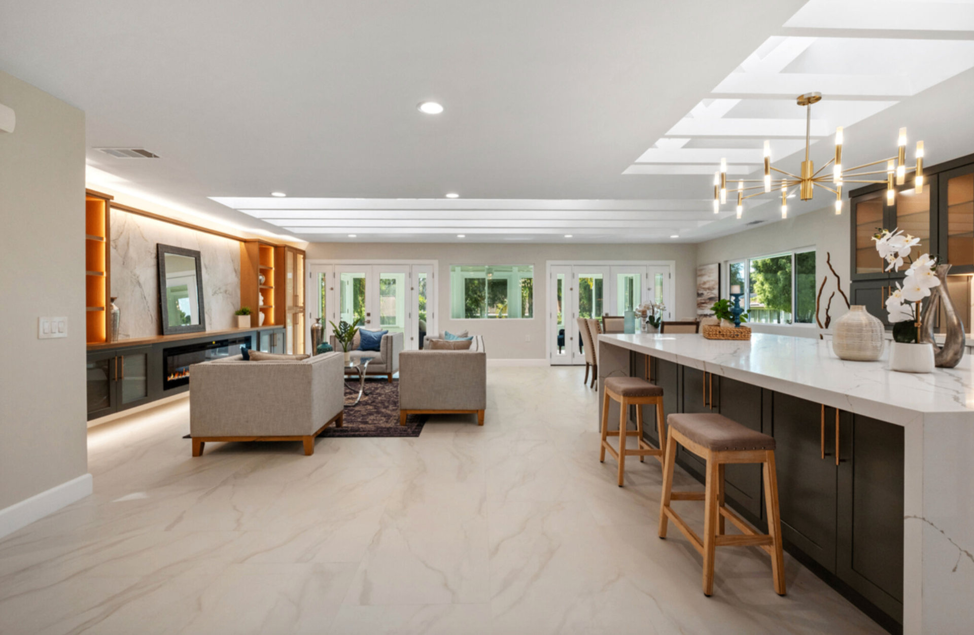 Open-concept great room with marble waterfall island, linear fireplace, and gold chandelier