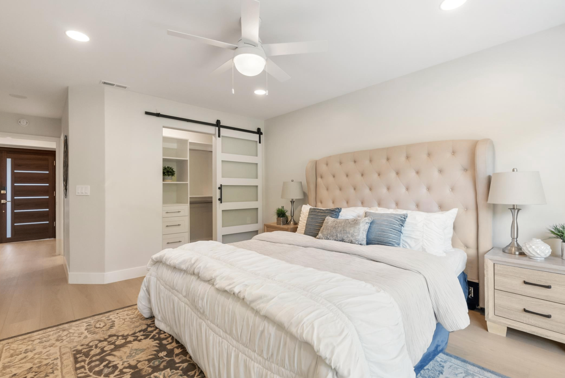 Primary suite with tufted headboard and sliding barn door leading to a custom walk-in closet