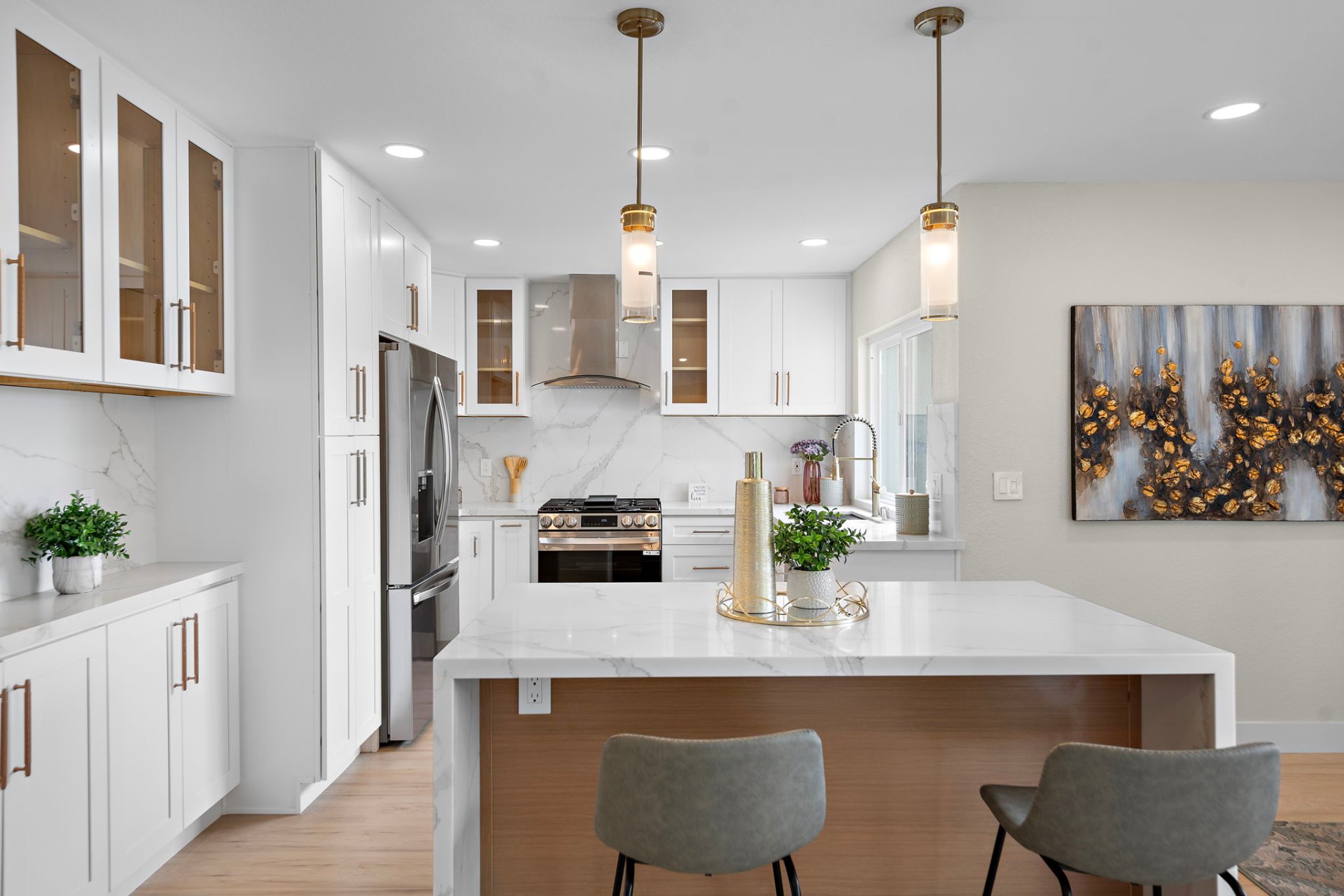 Bright white shaker kitchen with brass pendants, marble backsplash, and waterfall peninsula