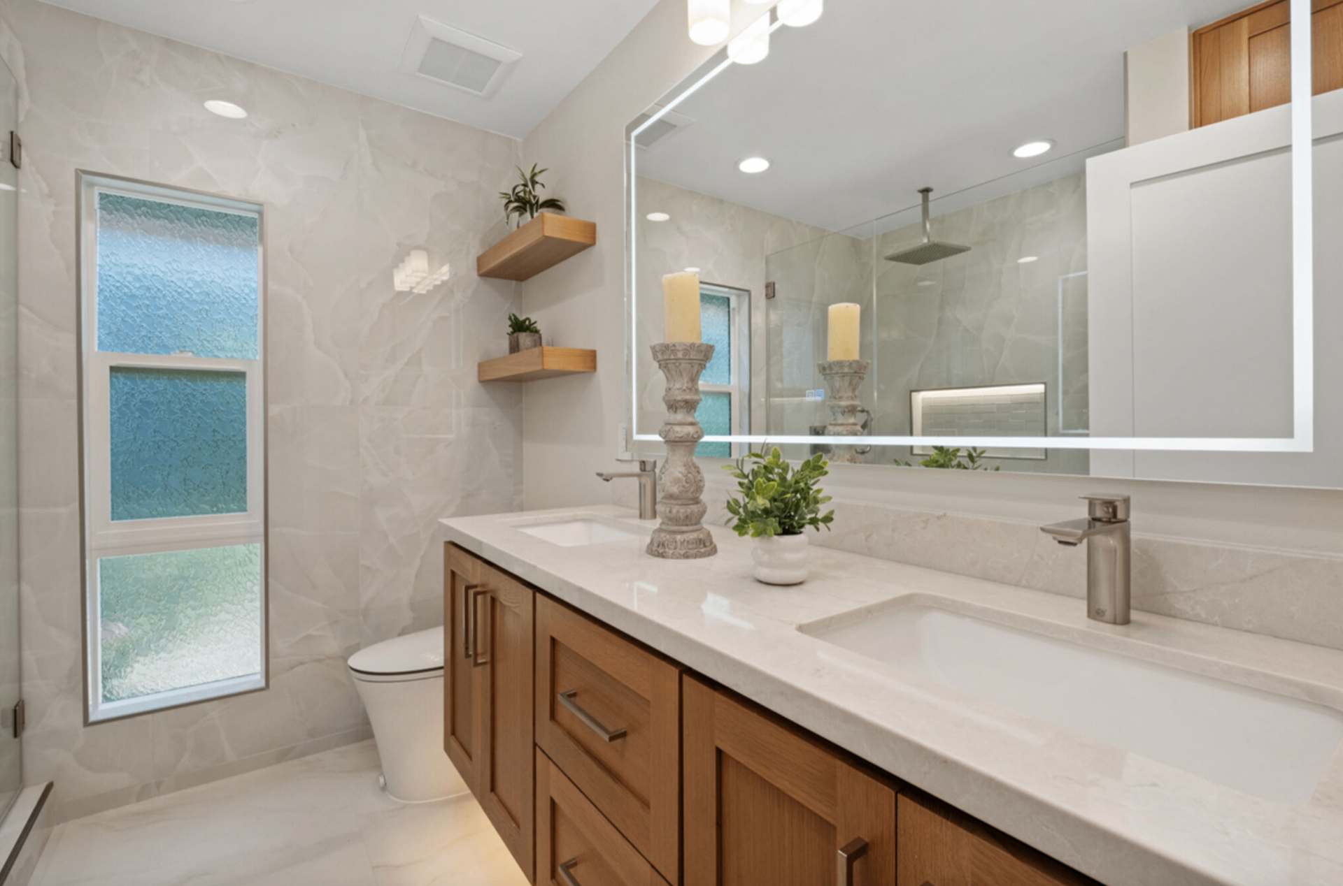 Bathroom with double vanity, warm oak cabinetry, quartz counters, and frameless glass shower